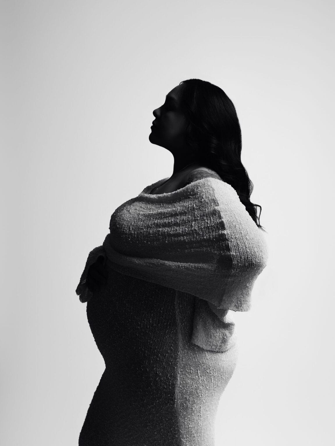 Silhouette maternity photo in studio with soft side lighting, showcasing baby bump in cozy knit dress.