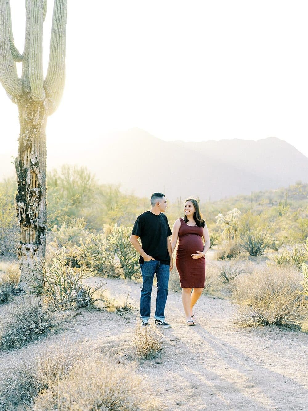 Outdoor maternity photoshoot in the Arizona desert at golden hour with couple walking hand-in-hand