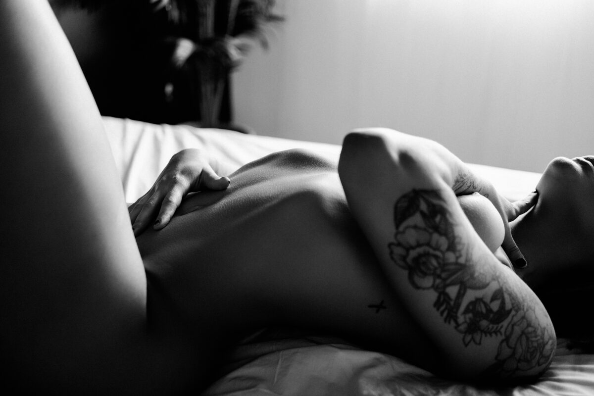 Indoor phoenix boudoir session on a bed with women holding her body with tattoos
