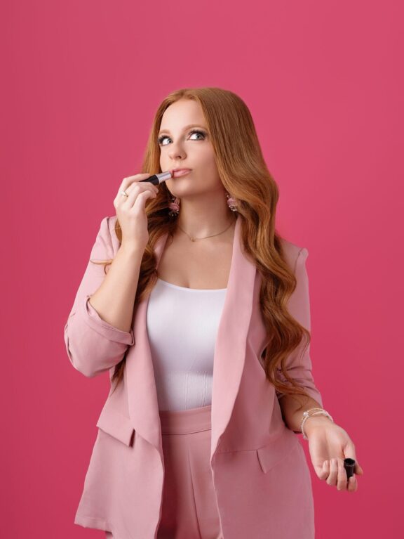 woman holding lipstick to her lips wearing full pink for her branding session