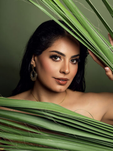 a beauty face shot of a beautiful indian woman peeking in between palm tree leaf