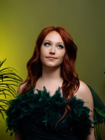 woman with red hair wearing a green dress and green backdrop like poison ivy