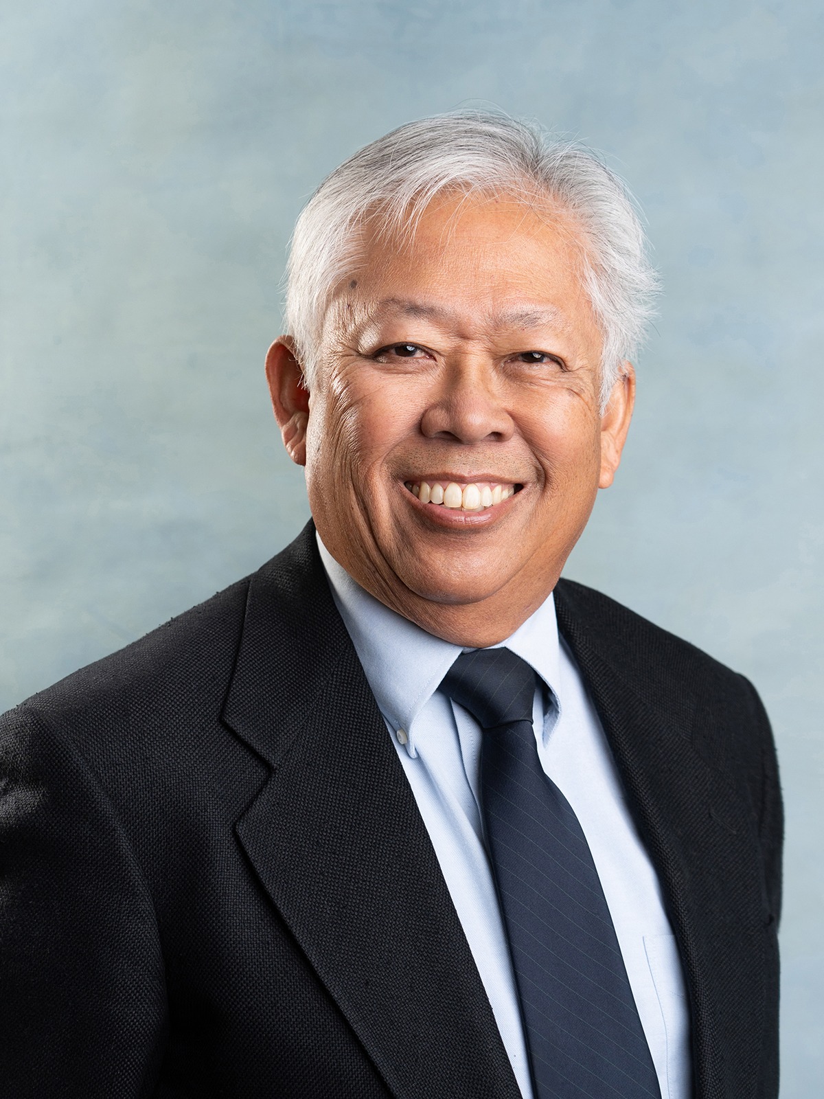 Classic business medical headshot of a smiling older man in a suit and tie on a light blue background