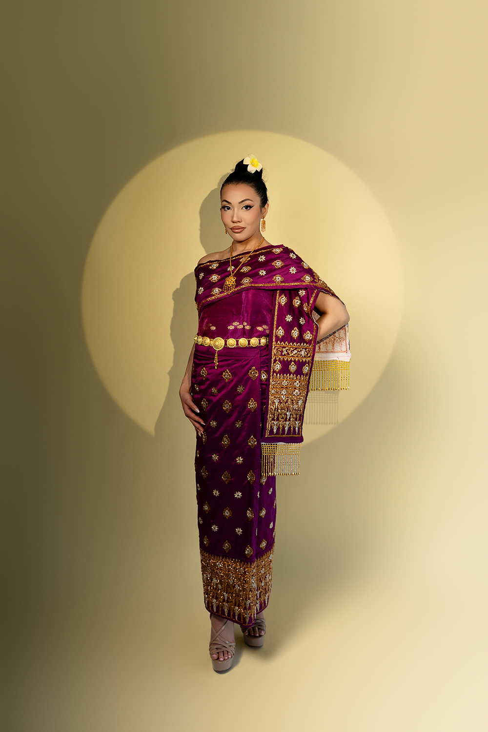 Full-body portrait of Miss USA International Arizona contestant in traditional Thai pageant attire, standing in spotlight on gold background