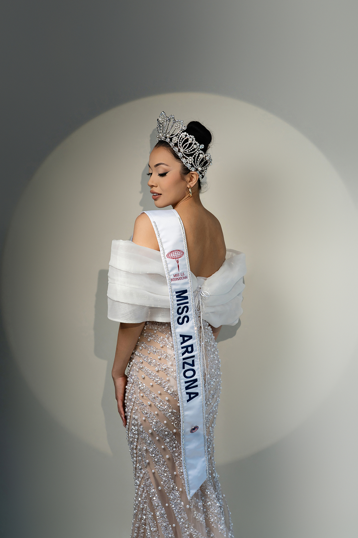 Back view of Miss Arizona contestant in Miss USA International crown and sash, wearing crystal gown with dramatic lighting