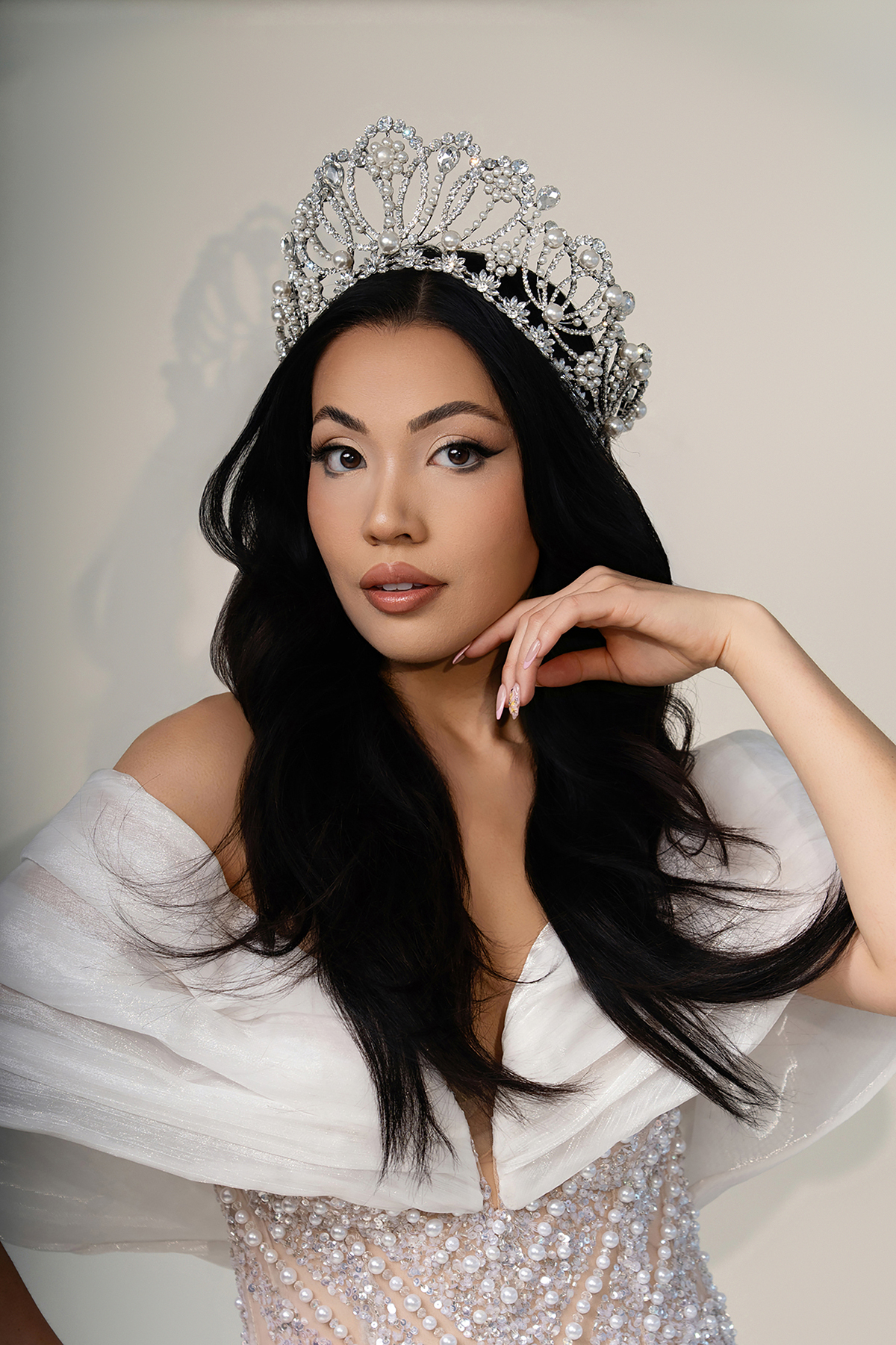 Glam headshot of Miss Arizona wearing crown and soft makeup, hand posed near chin, studio beauty lighting