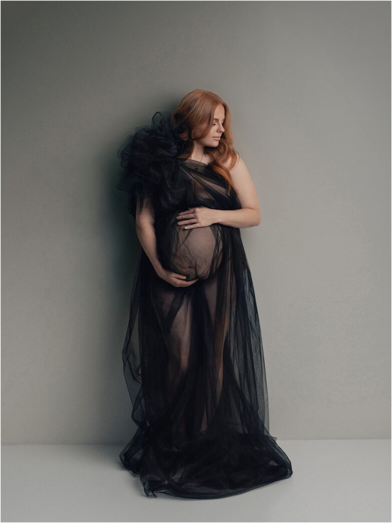 Pregnant woman wearing a sheer black maternity gown embracing her baby bump