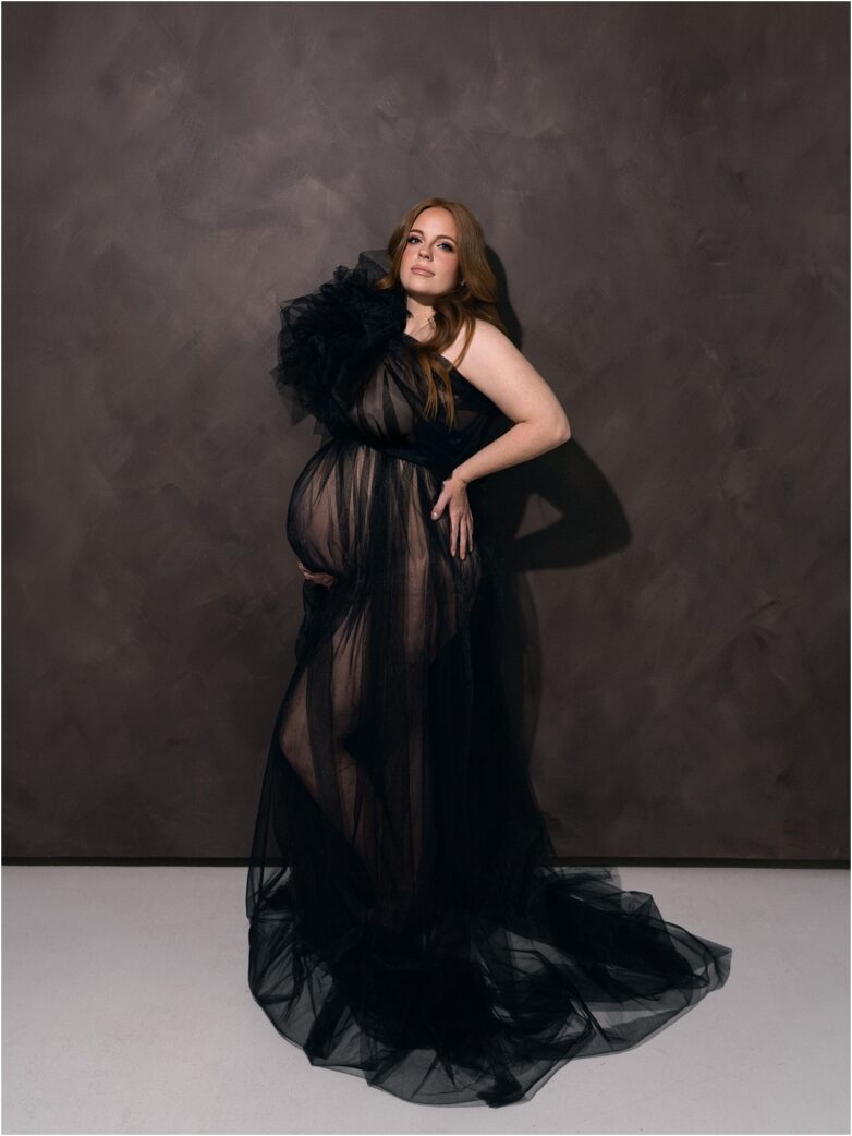 Pregnant woman wearing a dramatic black tulle maternity gown in studio