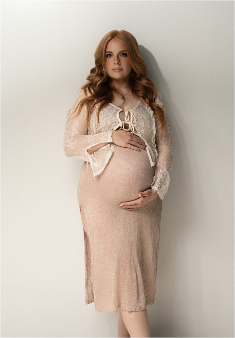 Expectant mother in a fitted beige maternity gown standing in studio