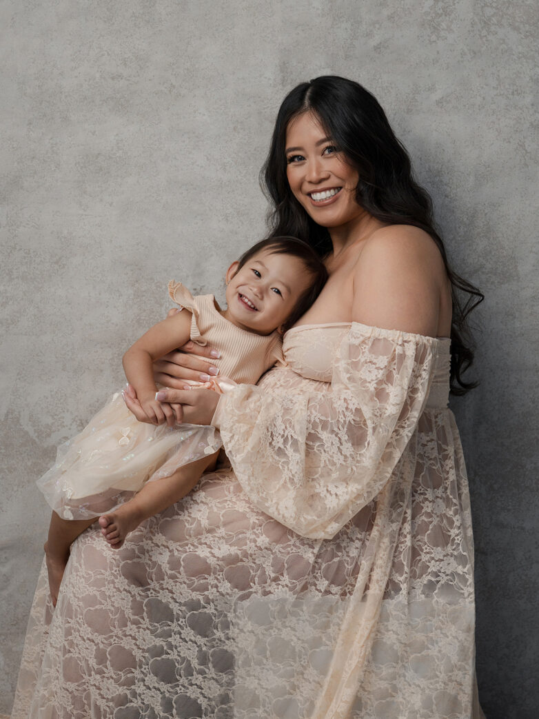 Mother in an off-shoulder cream gown hugging her daughter during a Phoenix maternity session